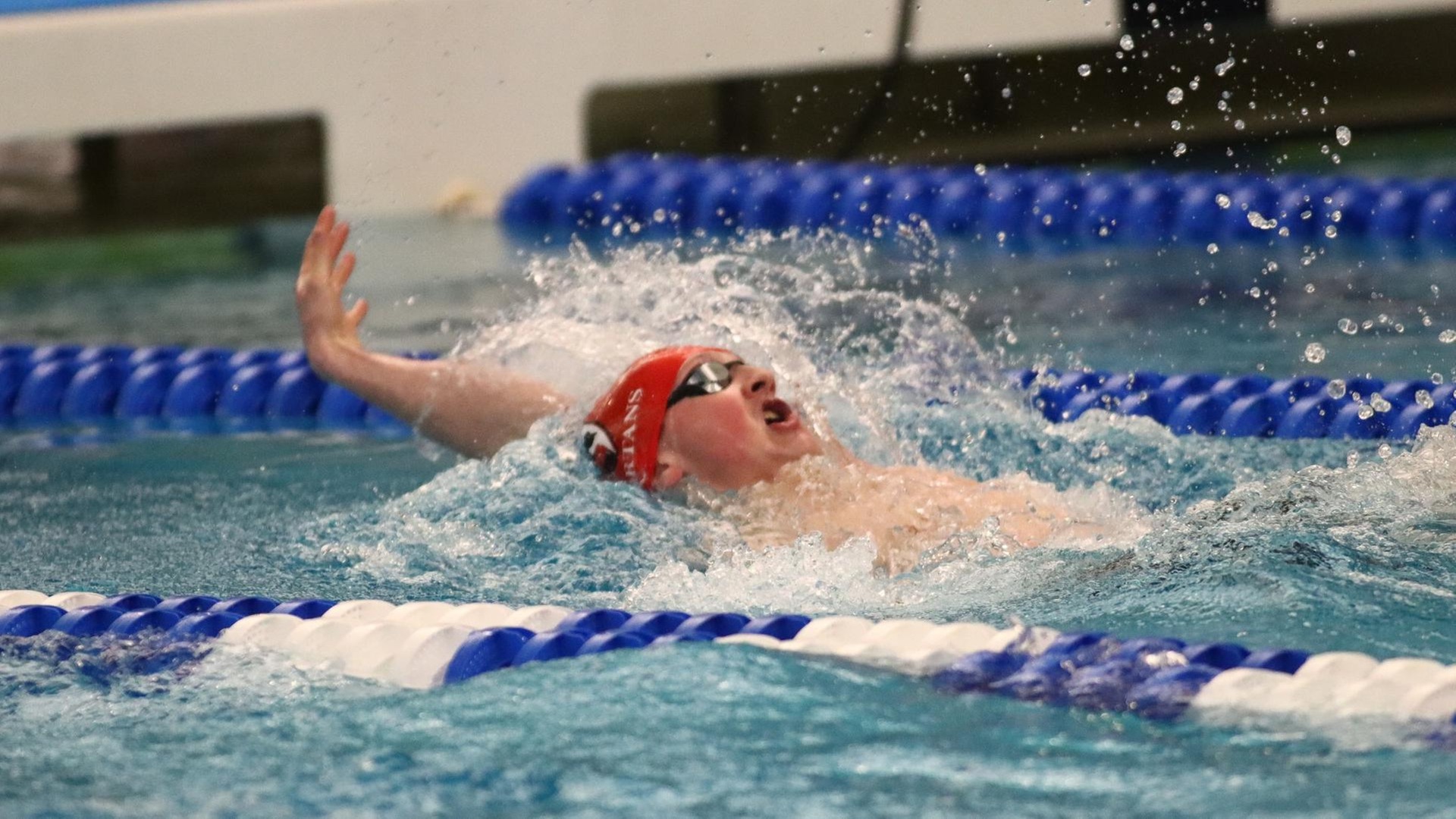 men's swimmer with a red cap on swimming the backstroke