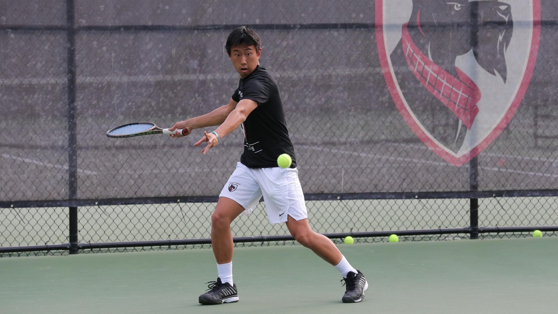 men's tennis player wearing a black shirt with white shorts about to swing his racquet