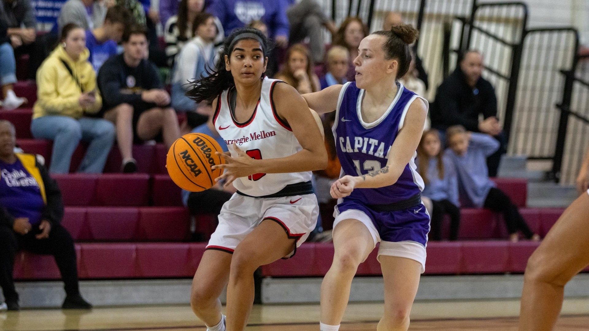 women's basketball player wearing a white uniform looks to pass or shoot with a defender wearing a purple uniform near her left shoulder