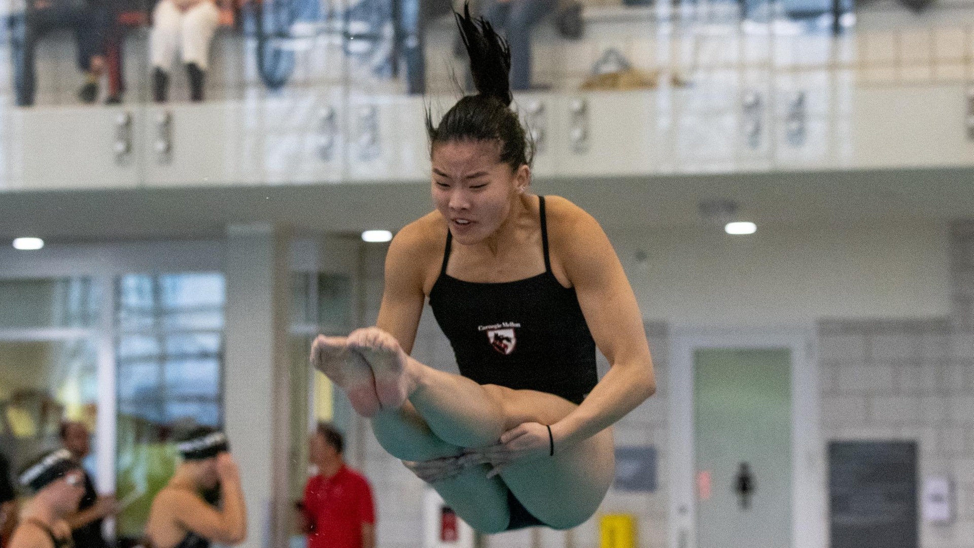 women's diver in air holding legs straight behind her knees