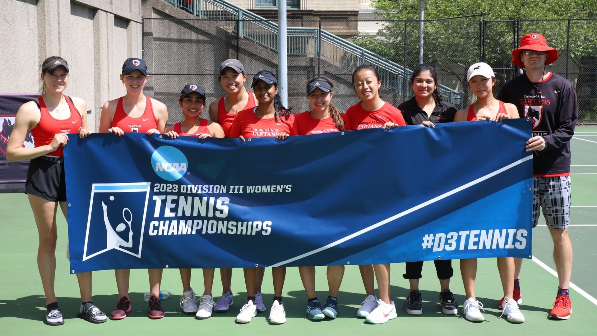 group photo of women's tennis team holding the NCAA championship banner and wearing red tank tops and black hats 