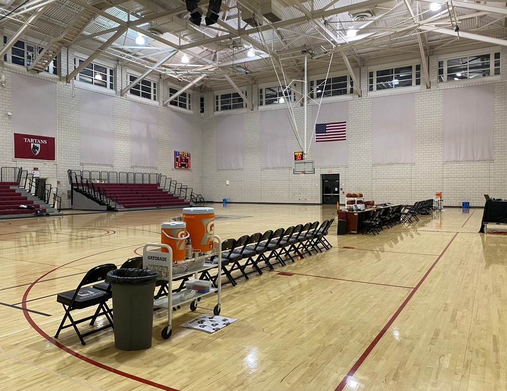 photo of basketball gym with chairs lined up and bleachers on far side