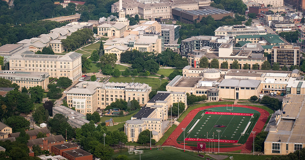 Aerial view of Carnegie Mellon campus includes numerous yellow brick buildings with football stadium