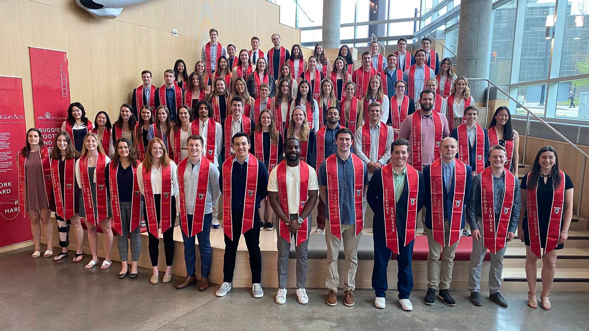 group of 60 students standing together with graduation sashes draped on necks