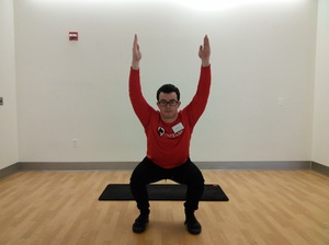 man in lower squat position facing forward with arms raised straight up