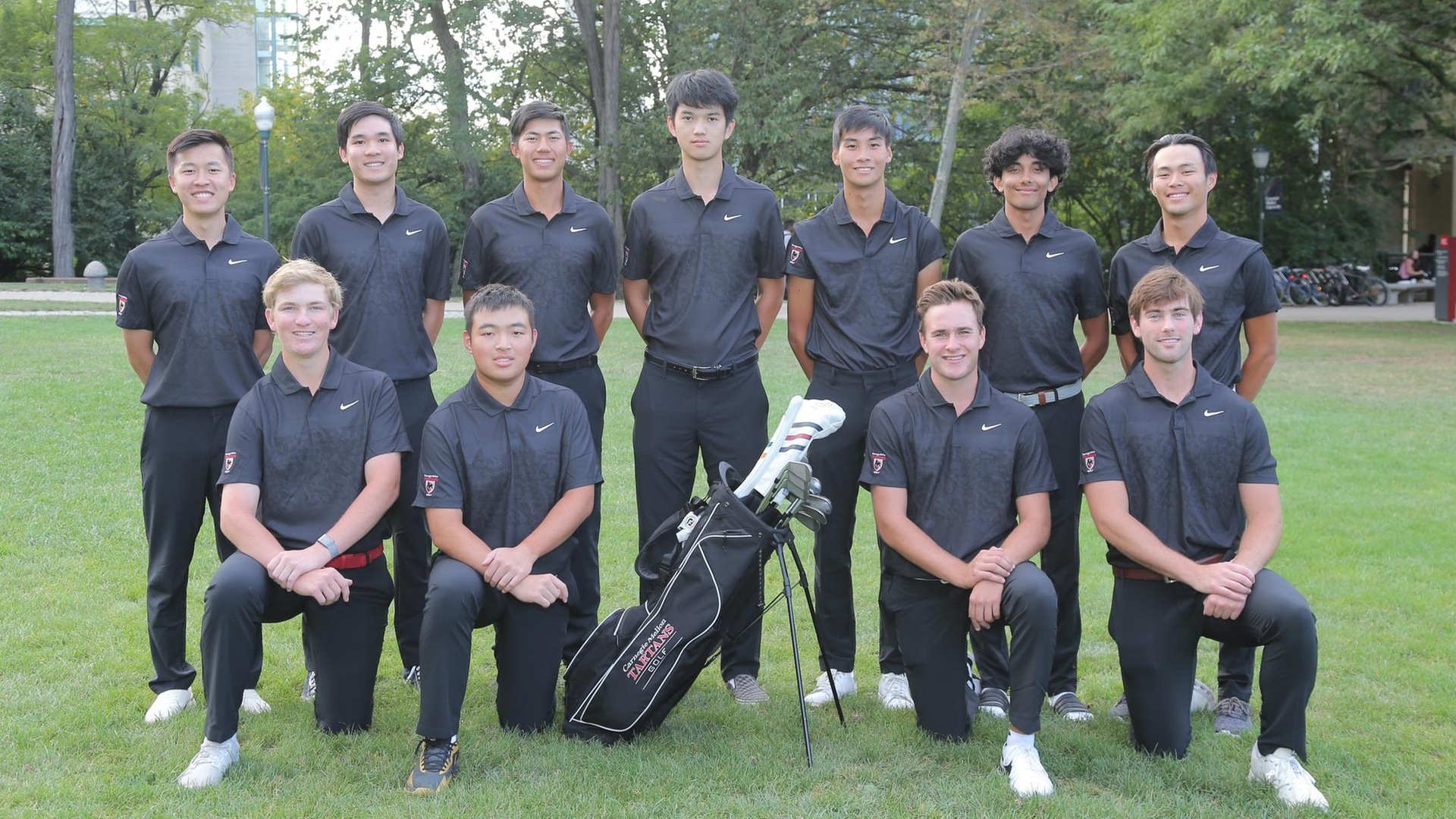 men's golf team photo with players wearing black shirts and black pants with one row kneeling and one row standing