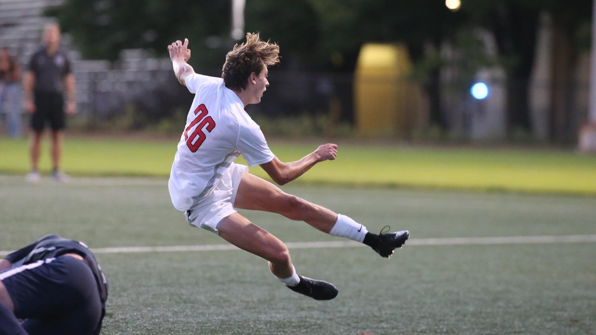 men's soccer player wearing white uniform off the ground after kicking the ball