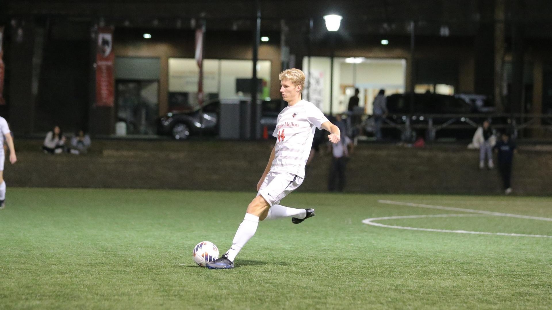 men's soccer player wearing a white uniform prepares to strike the ball with his right foot