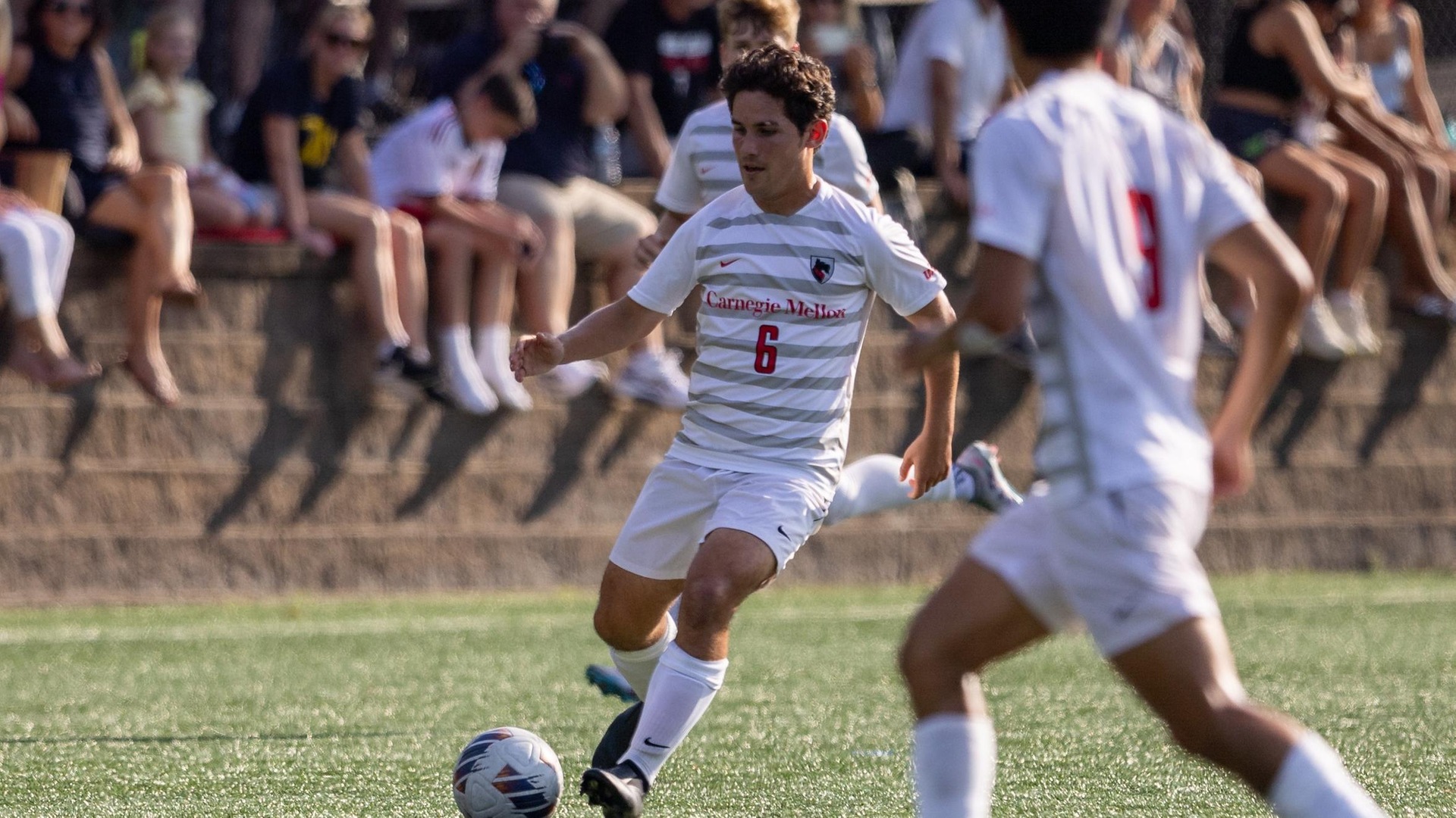 men's soccer player wearing a white uniform pulls leg back to kick the ball near his left foot