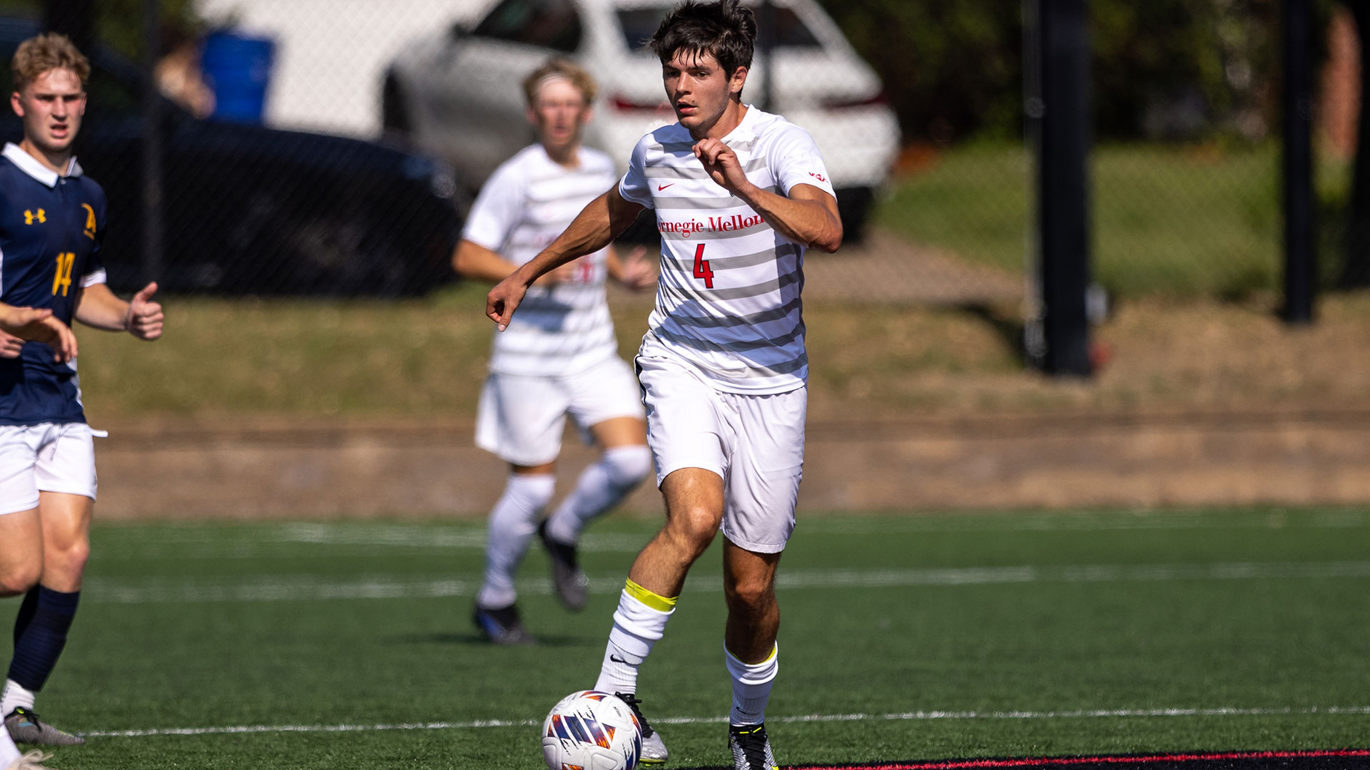 men's soccer player wearing white uniform dribbling ball with outside of right foot