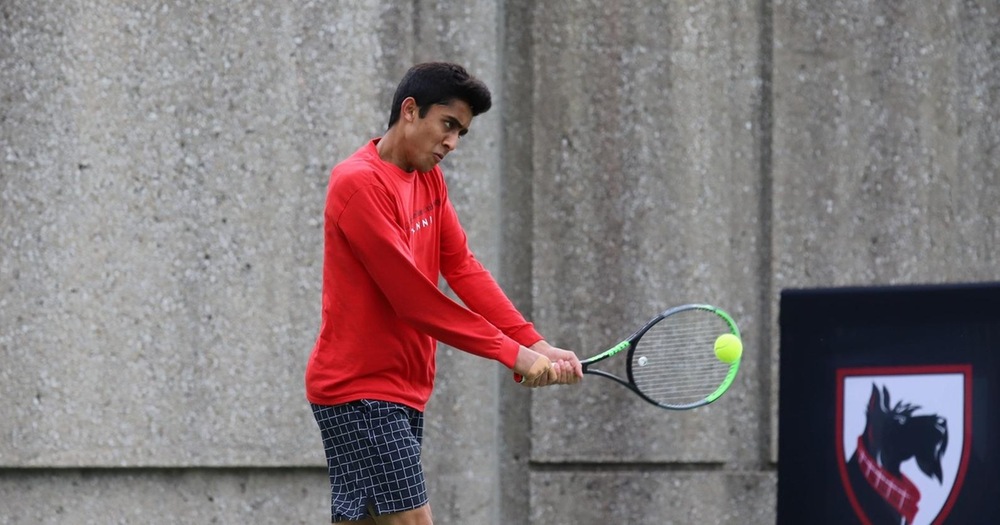 men's tennis player wearing red shirt and black shorts strikes the ball