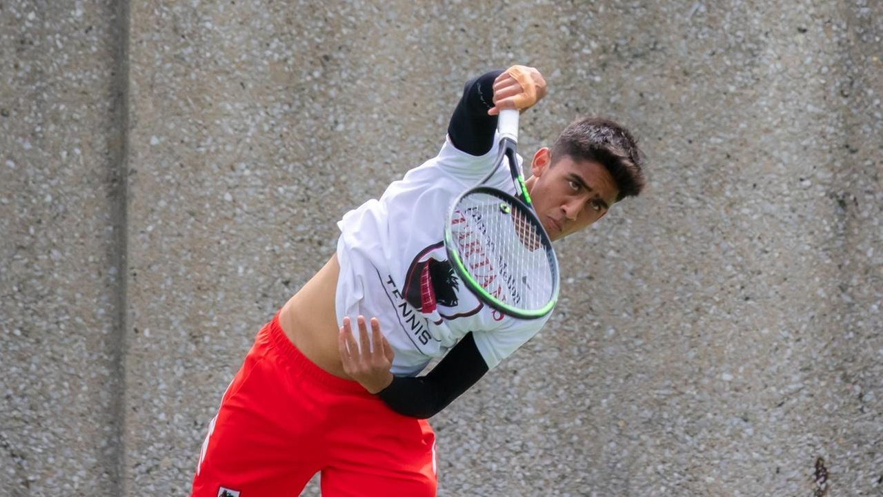men's tennis player wearing white shirt and red shorts staring forward after a shot