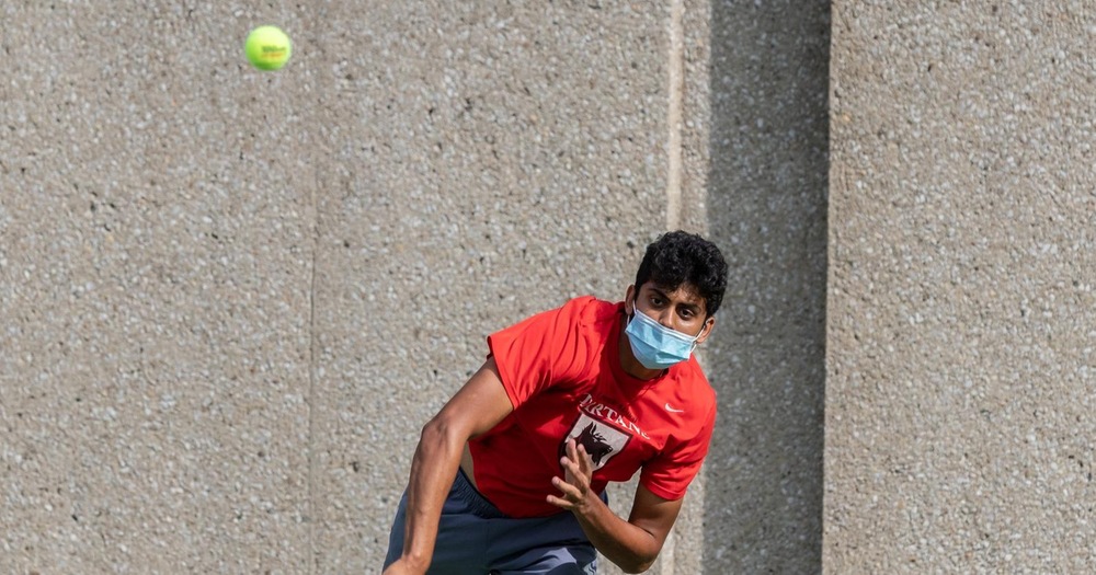 men's tennis player wearing red shirt in follow-through from serve