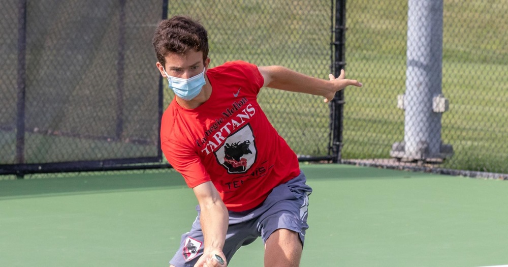 men's tennis player wearing red shirt and gray shorts swinging low