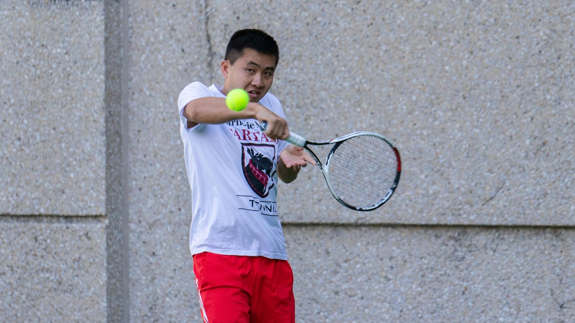 men's tennis player wearing a white shirt and red shorts prepares to hit a ball