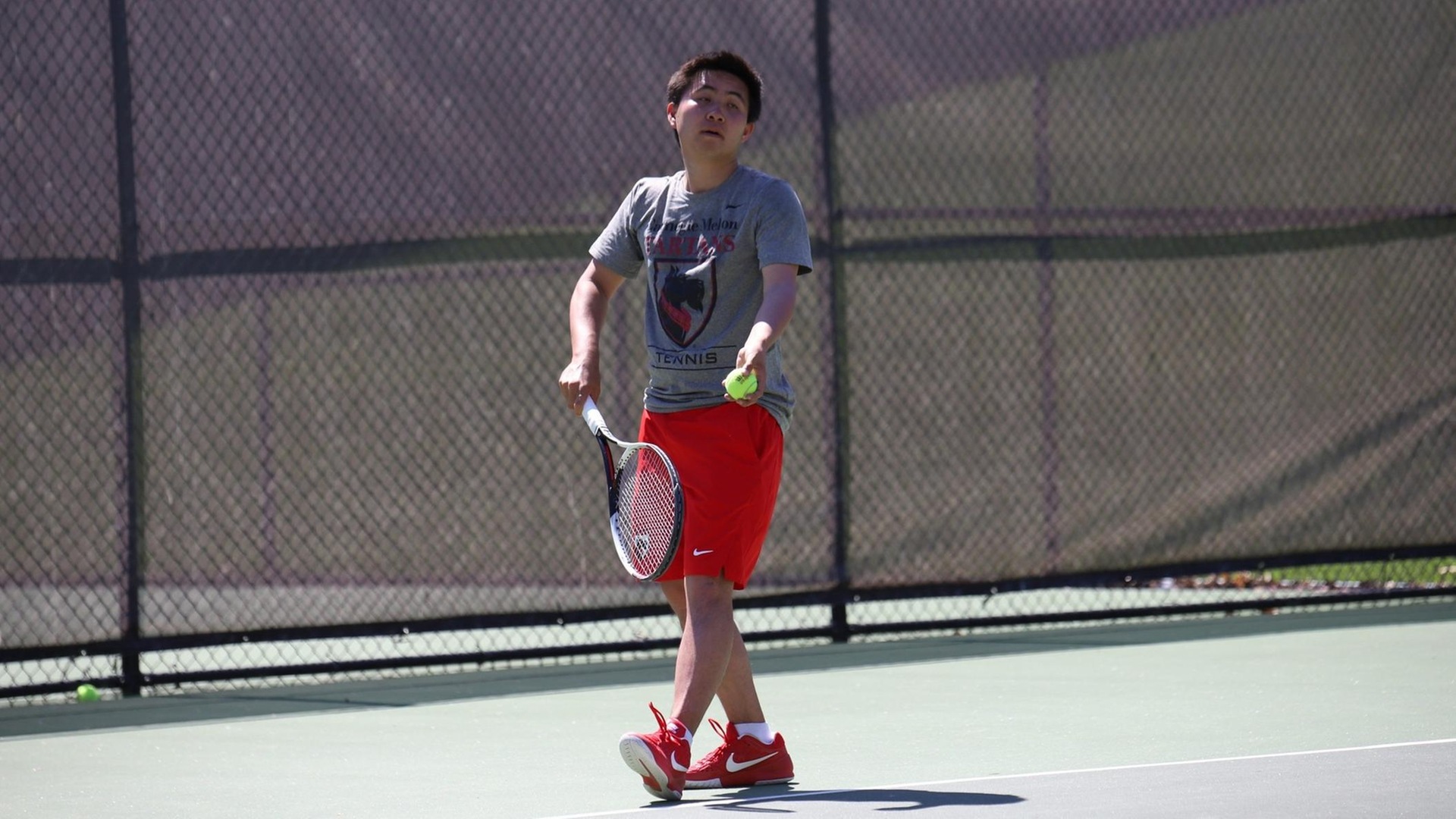 men's tennis player wearing gray shirt and red shorts about to serve