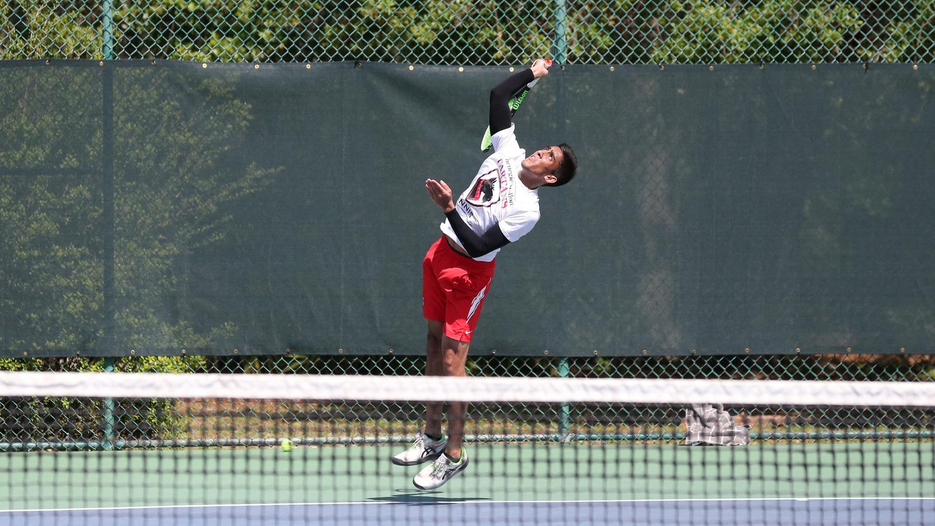 men's tennis player wearing a white shirt and red shorts in serving motion