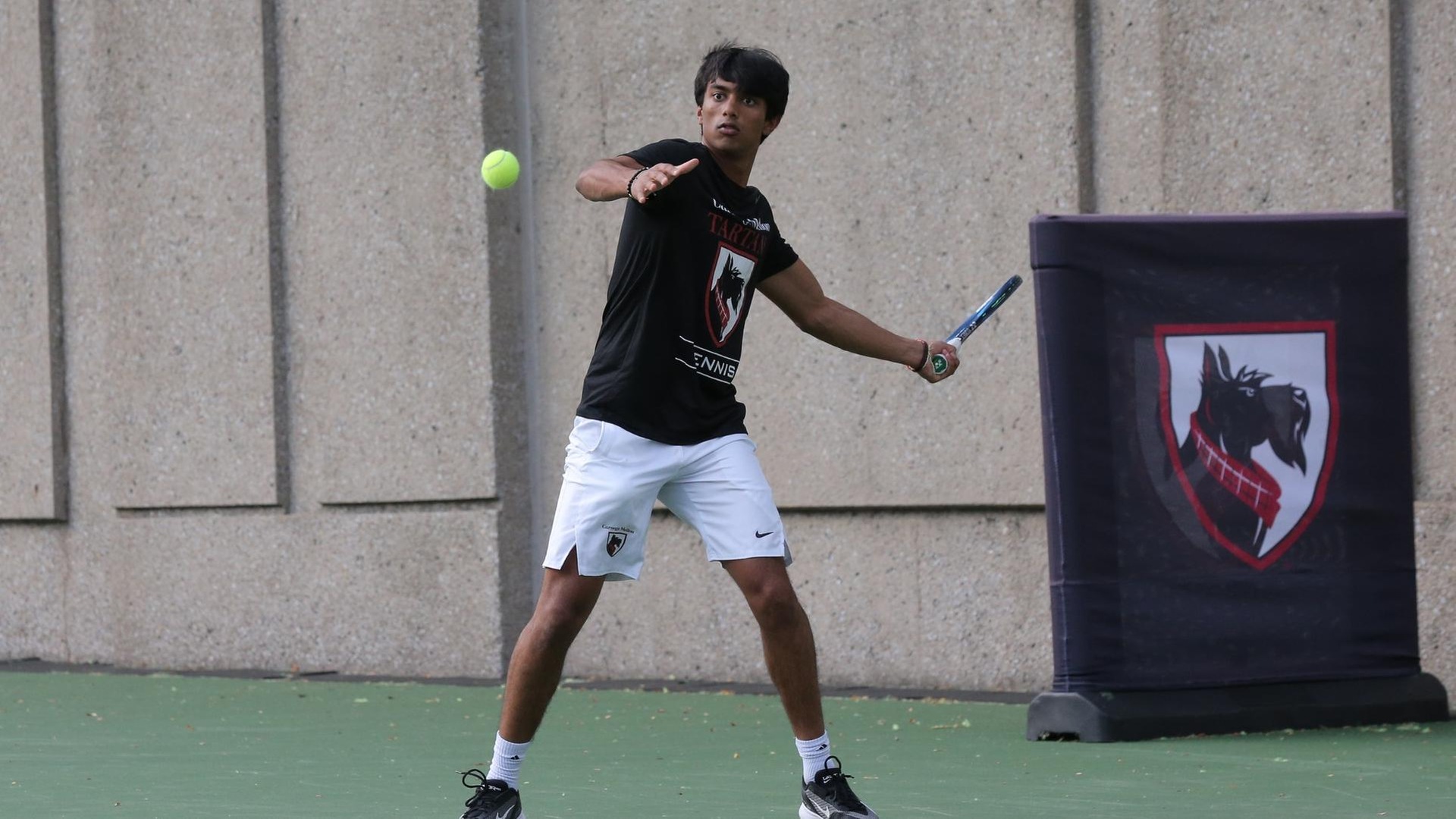 men's tennis player wearing a black shirt and white shorts swings racquet at the ball