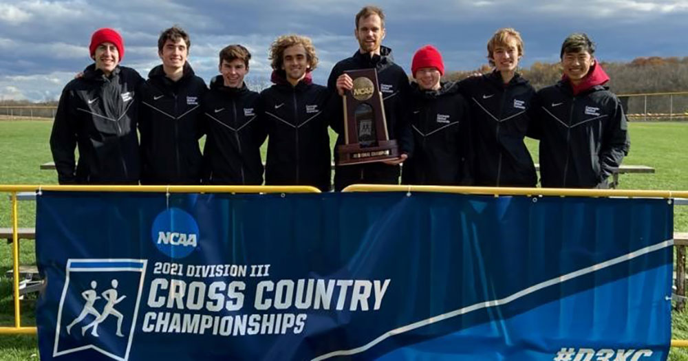 group photo of eight men's cross country runners standing behind a banner with a trophy in hand