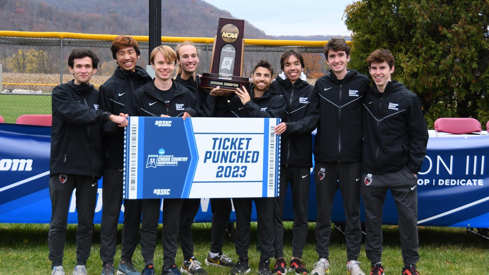 group of men wearing black training suits holding a trophy and sign reading Ticket Punched 2023
