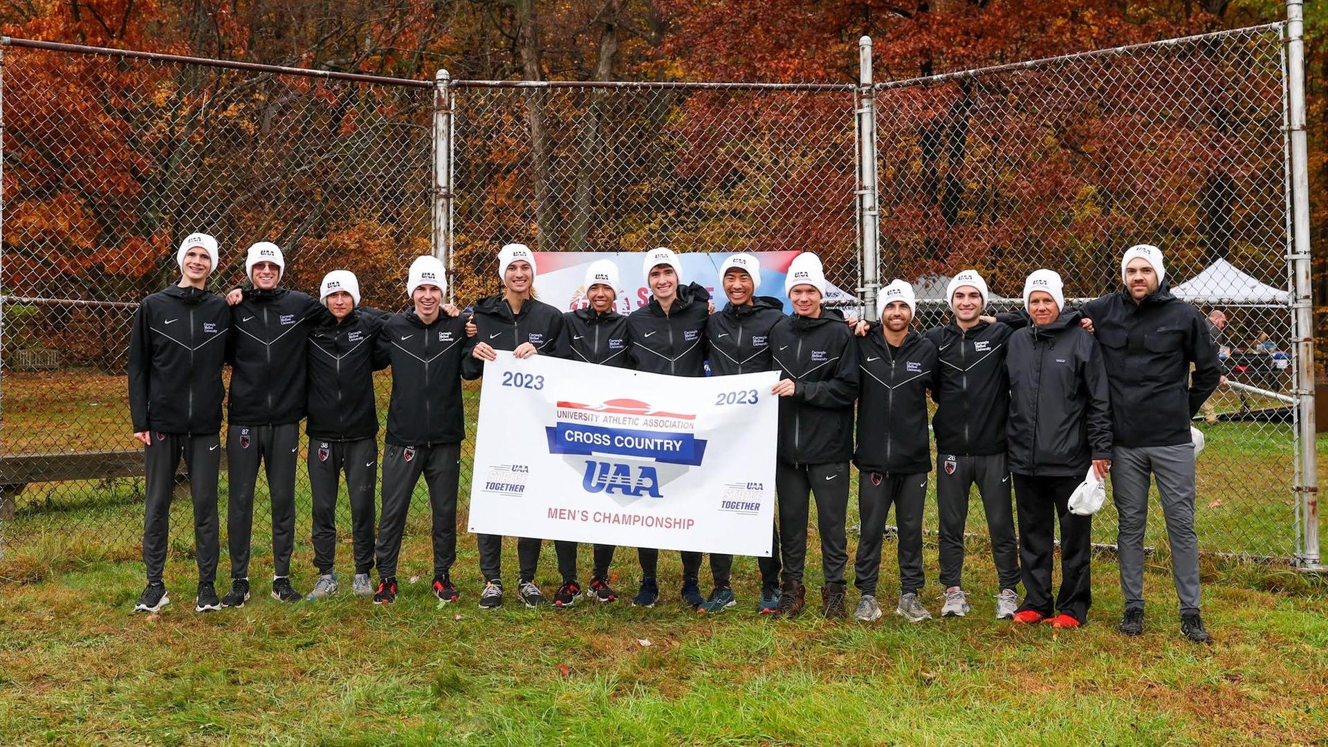team photo of men wearing black jackets and pants with white winter hats and holding a banner reading UAA Men's Cross Country Championship