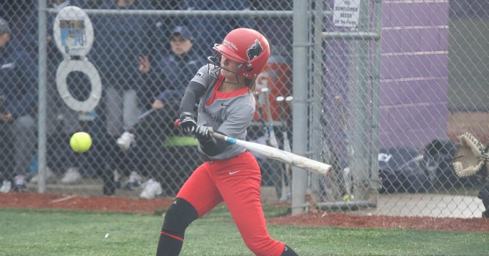 women's softball player wearing a gray uniform top and red pants swinging at a pitch