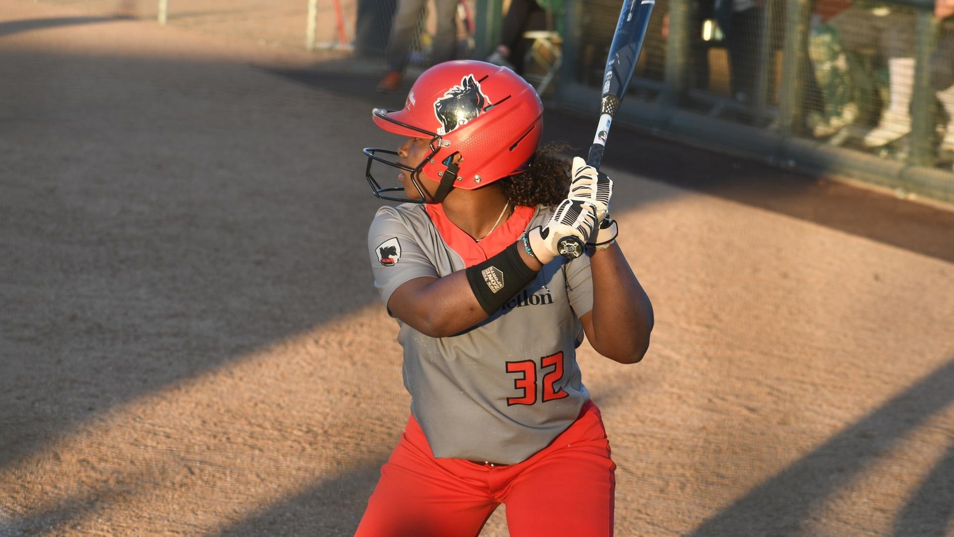 softball player wearing gray shirt and red pants standing at the plate
