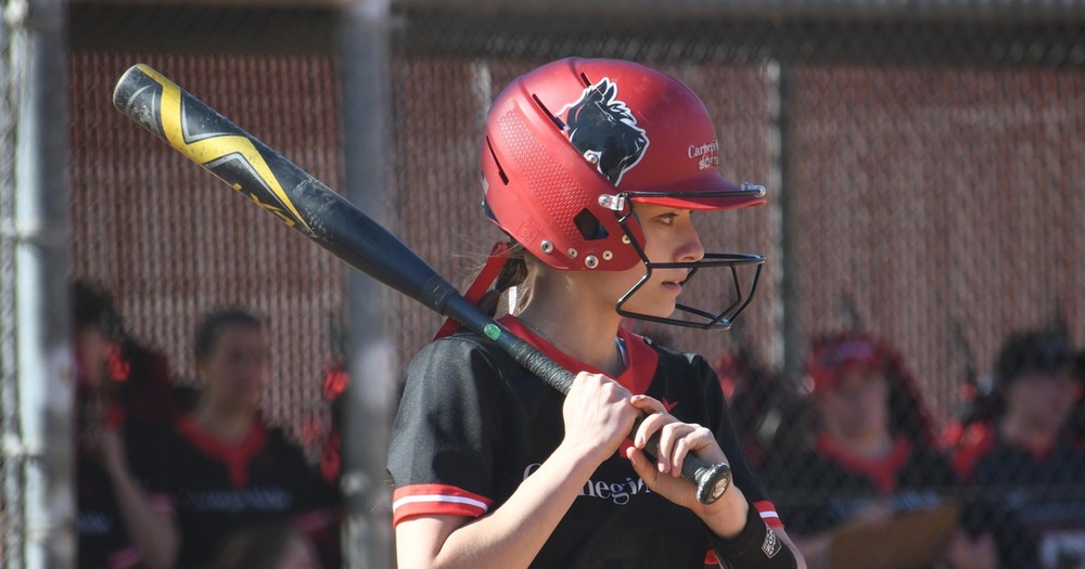 women's softball player standing with bat on shoulder looking out toward the field