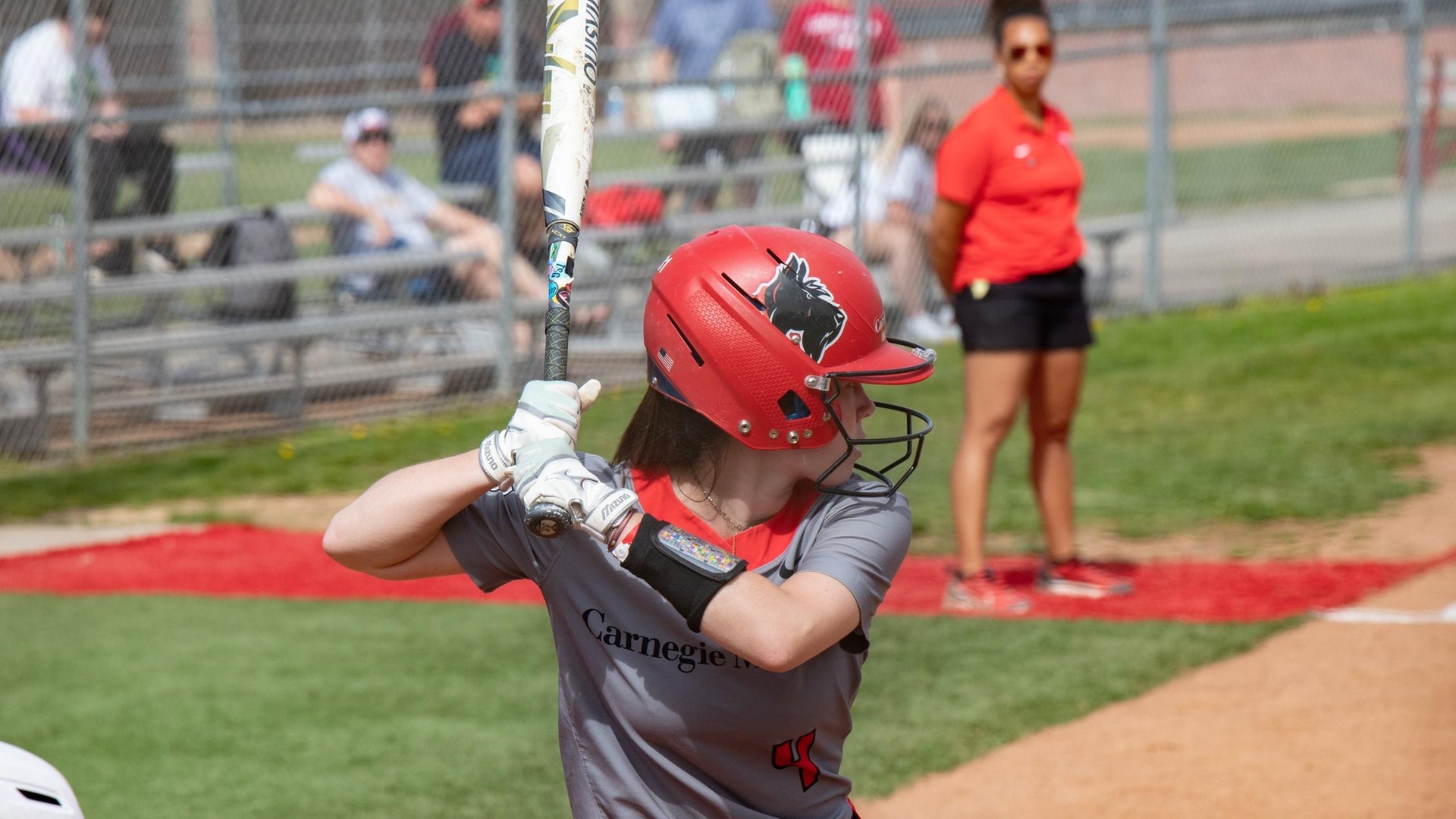 softball batter wearing a gray uniform jersey and red helmet at the plate ready for the pitch