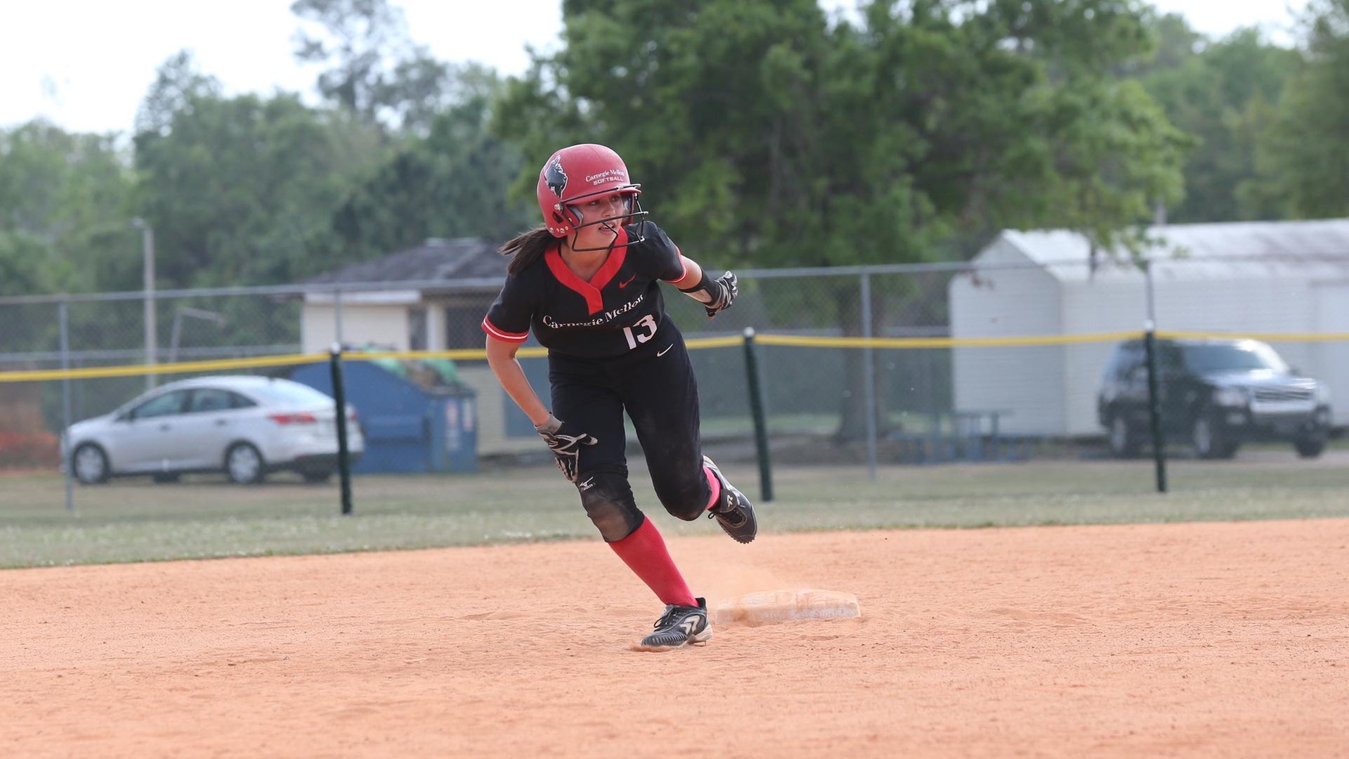 women's softball player wearing all black uniform with red trim running off second base