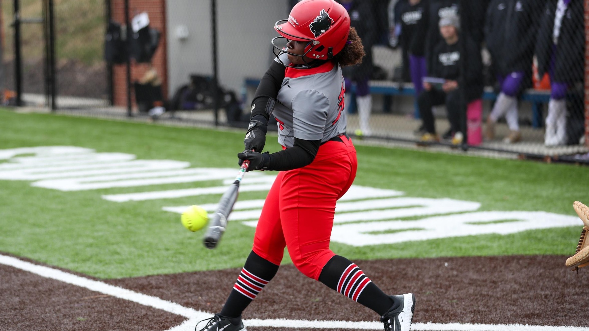 women's softball player batting left-handed and swinging the bat to meet the ball