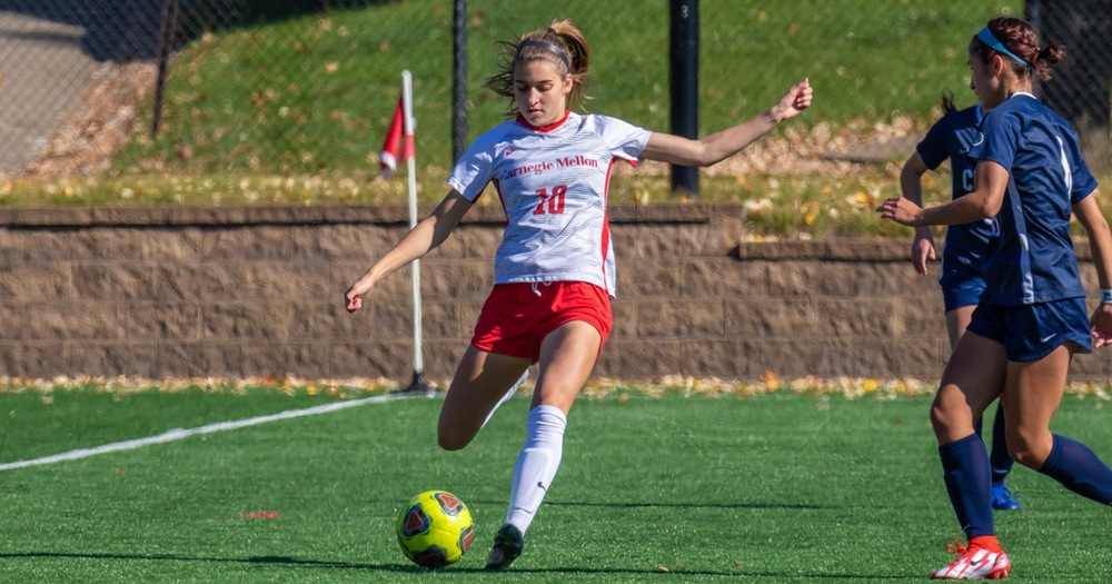 women's soccer player wearing white shirt and red shorts prepares to kick the ball
