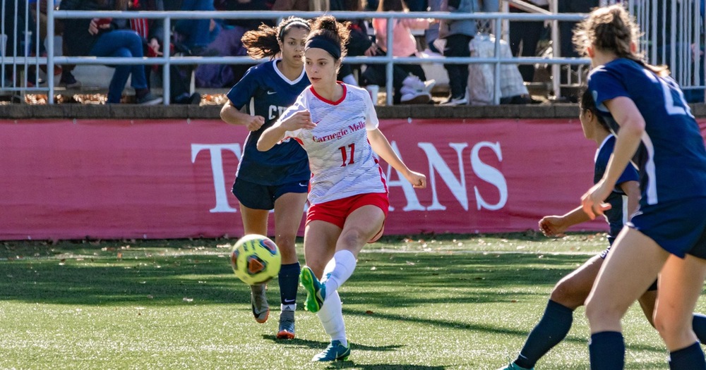 women's soccer player wearing white striking a ball with defenders on either side