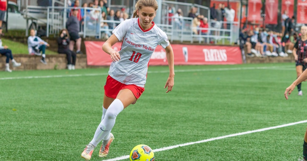 women's soccer player wearing white shirt and red shorts running forward with the ball
