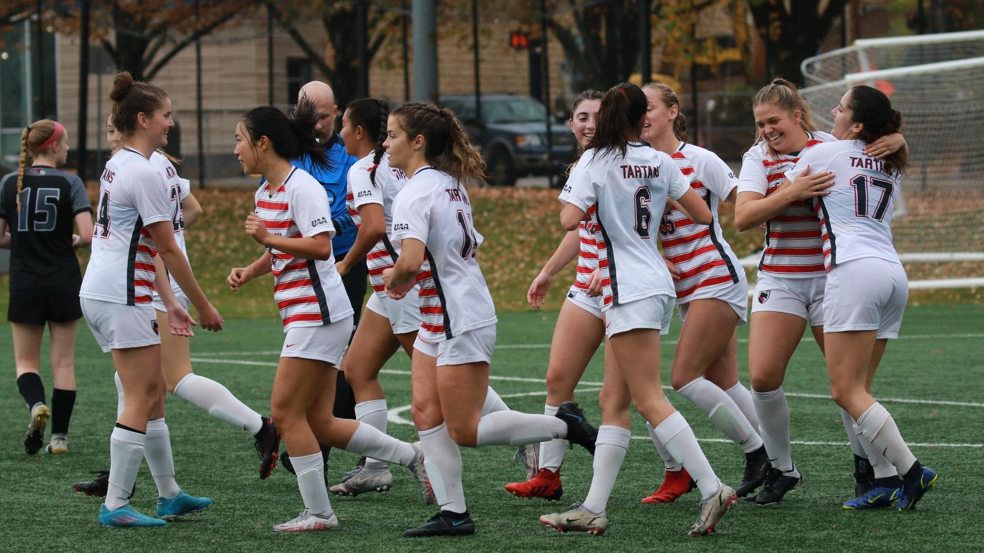 women's soccer players wearing white uniforms smiling together after scoring a goal