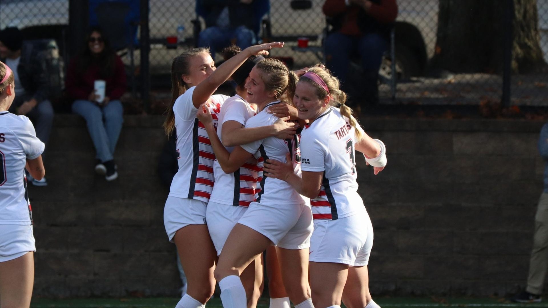 group of women's soccer players hugging in celebration after scoring a goal