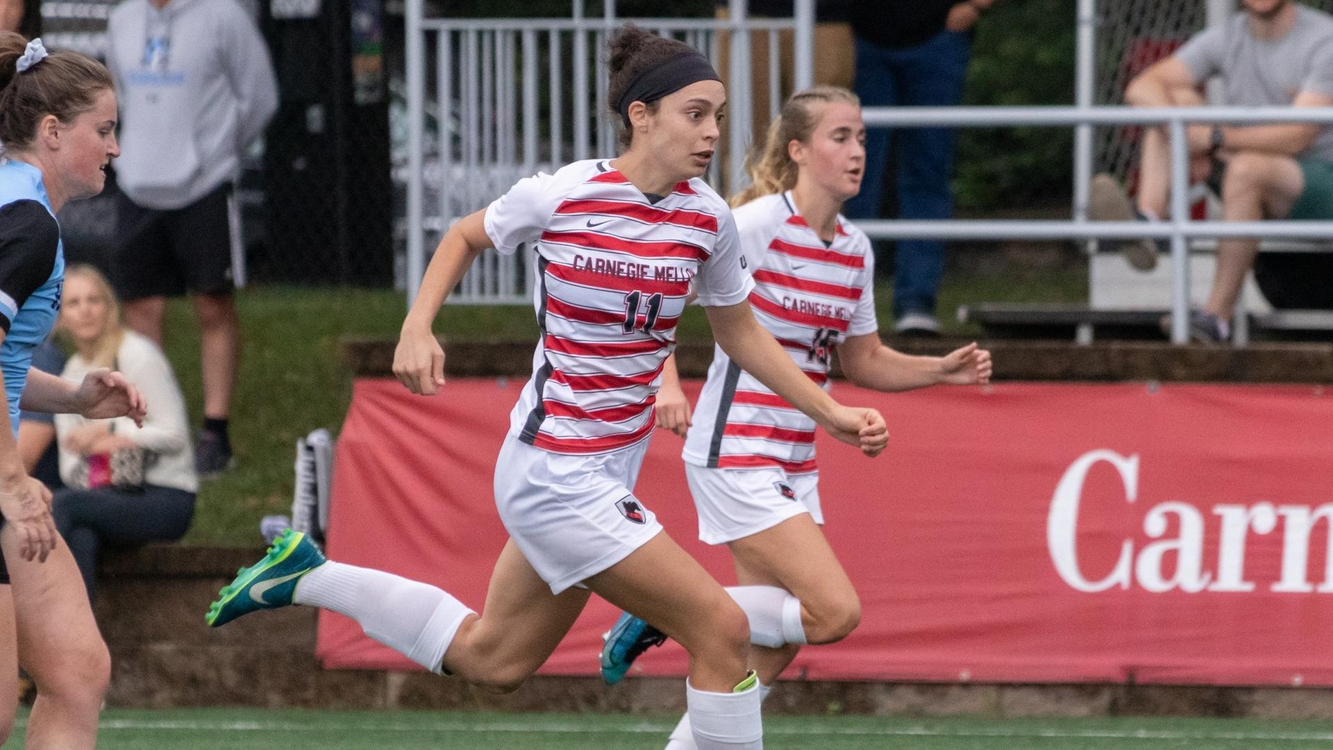 women's soccer player wearing white and red striped shirt and white shorts running with ball at foot and teammate to the left with a defender chasing