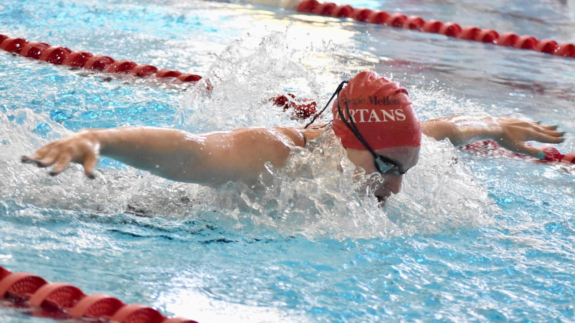 women's swimmer in red cap with arms stretched out doing butterfly stroke