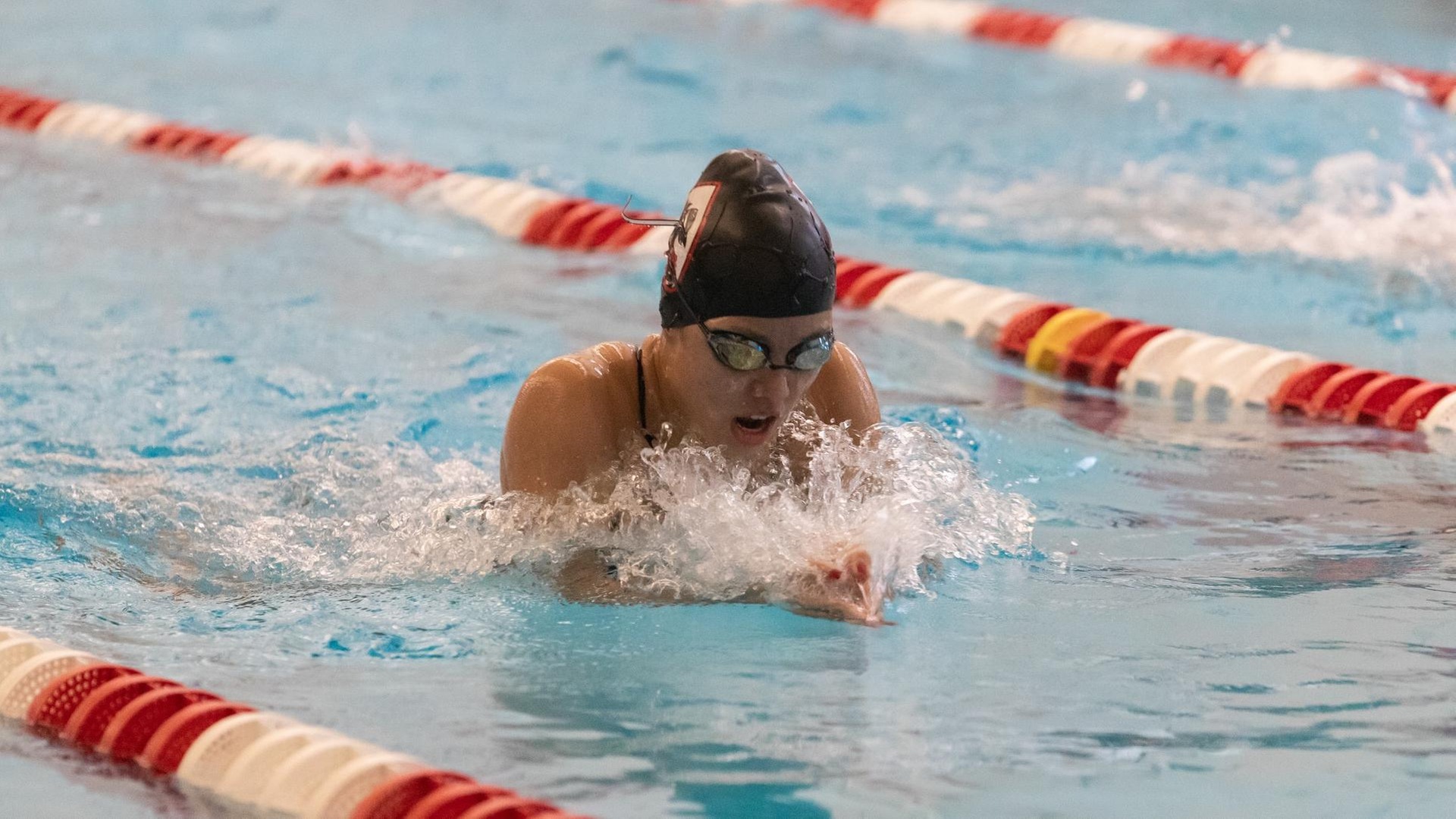 women's swimmer doing the breaststroke with head out of water wearing a black swim cap