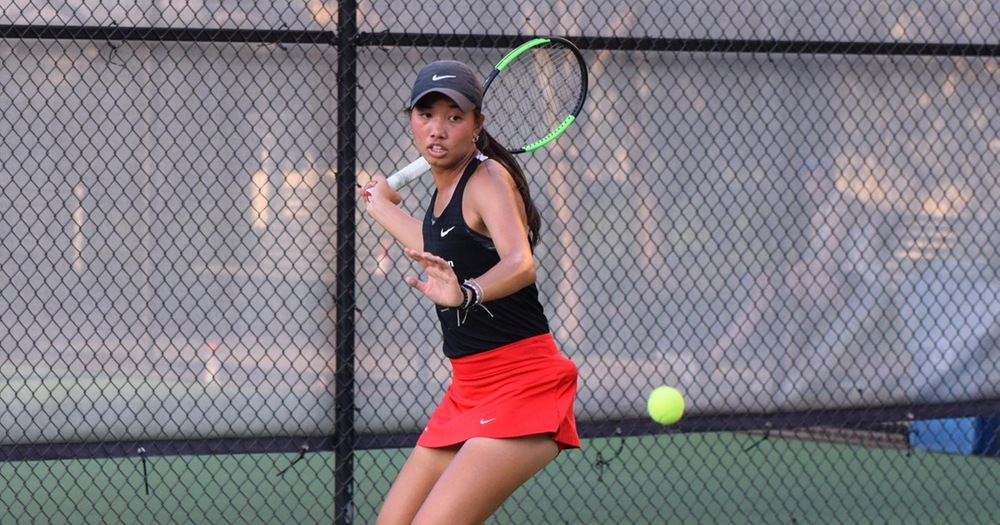 women's tennis player wearing black shirt and red skirt returning a shot