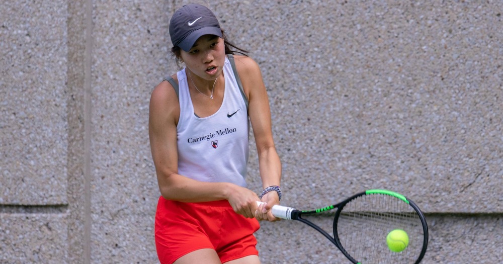 women's tennis player wearing white tank top, red shorts, and black hat hitting a tennis ball