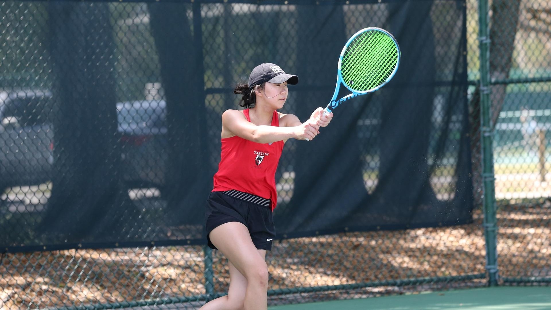 women's tennis player wearing red top and black shorts swinging the racquet