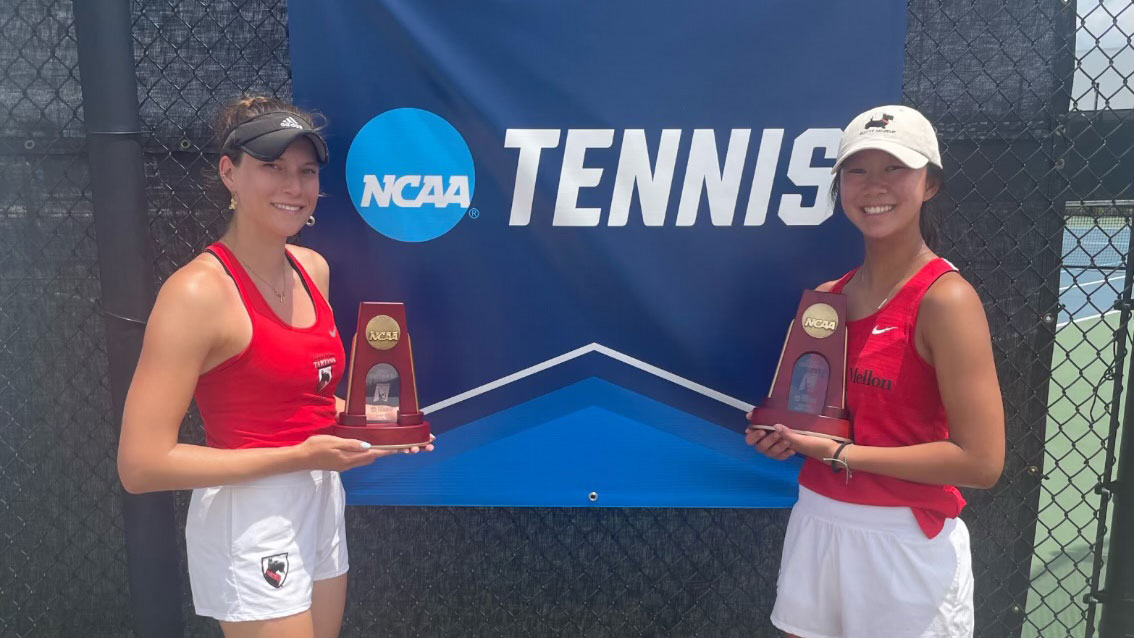 two women wearing red tank tops and white shorts holding trophies next to NCAA Tennis banner