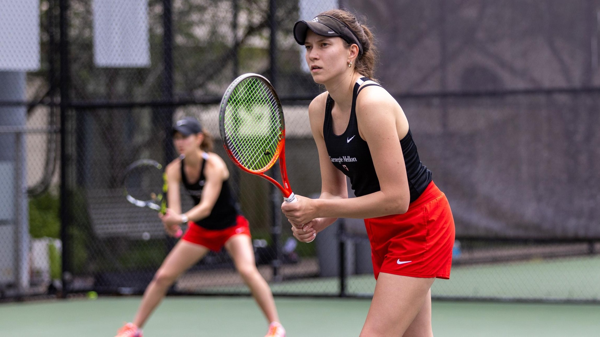 women's tennis player wearing a black top and red shorts holding a racquet