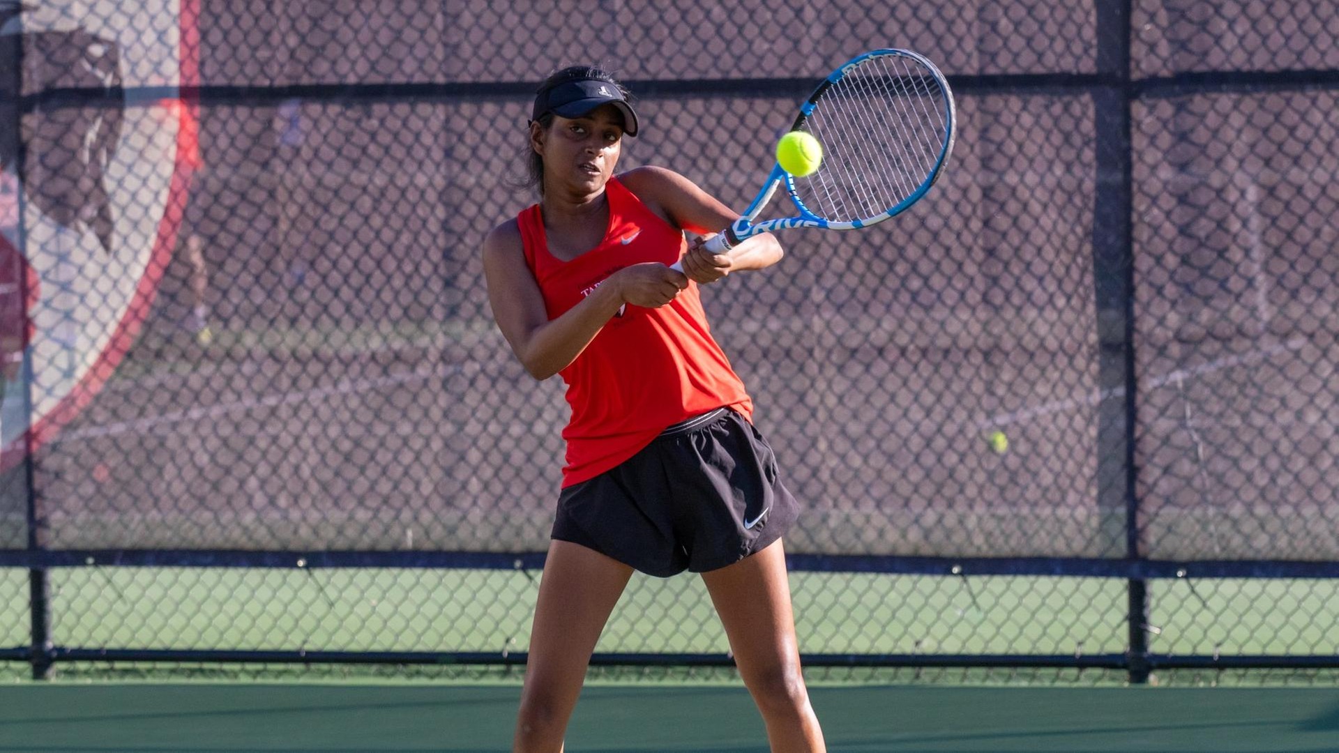 women's tennis player wearing red tank top and black shorts swing racquet at the ball
