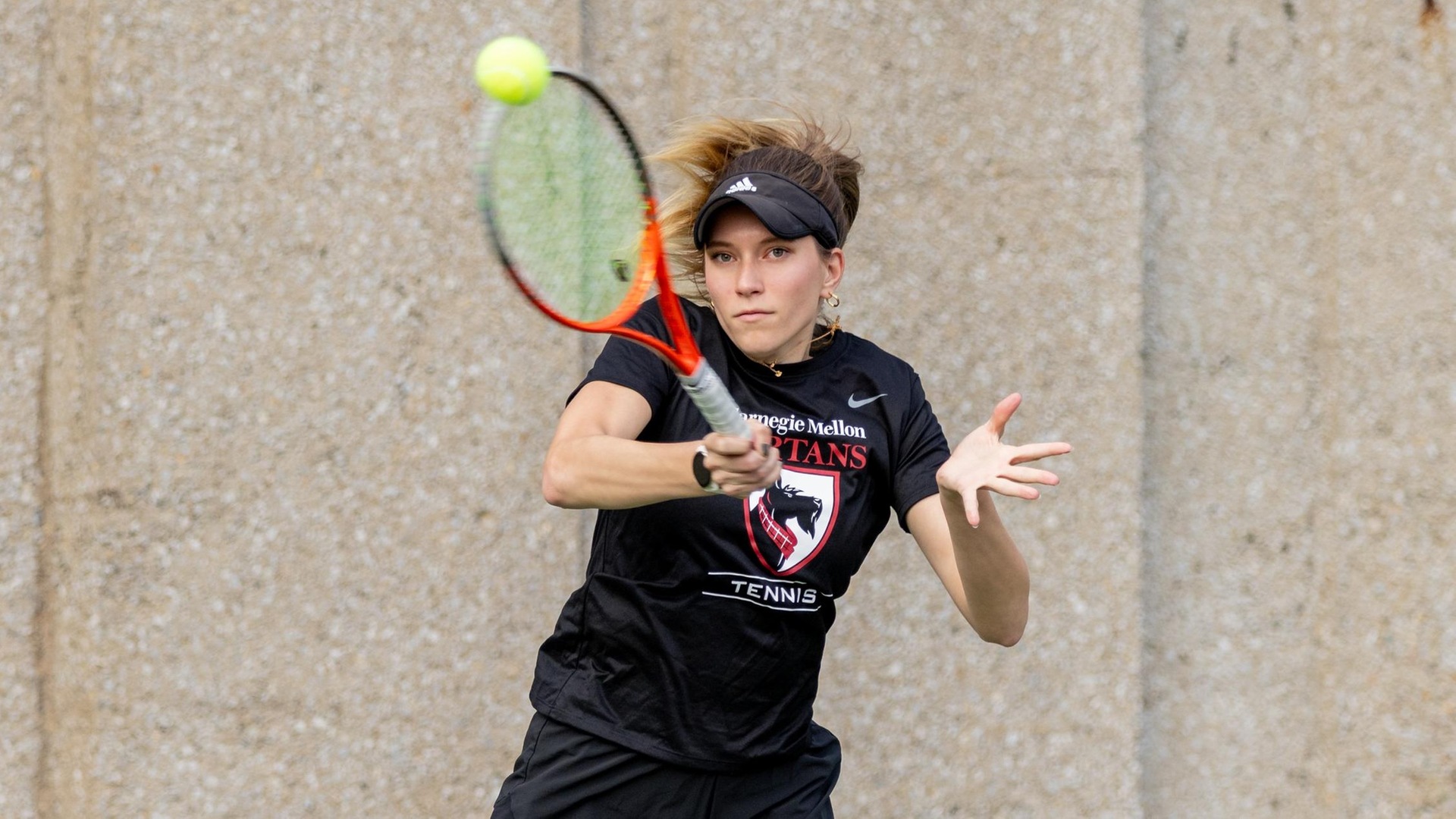women's tennis player wearing black shirt and black shorts swings racquet at ball