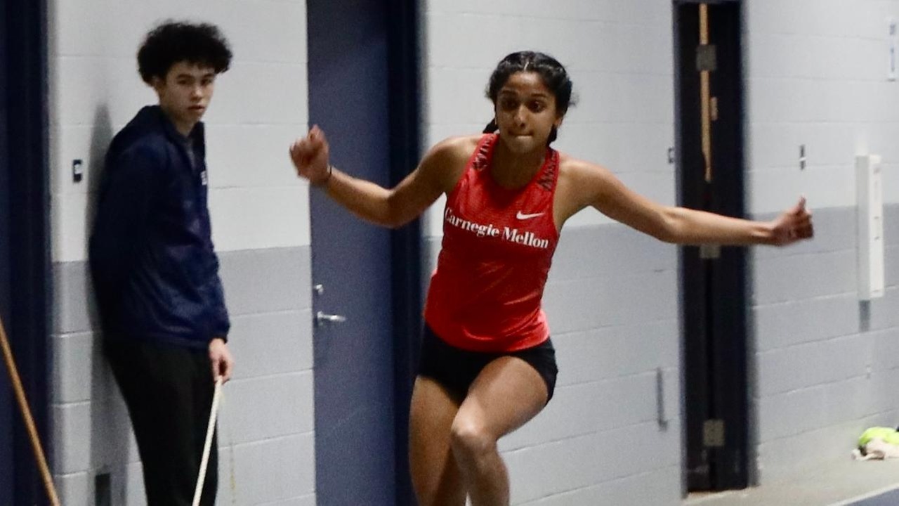 women's track athlete wearing a red jersey and black shorts jumps down runway for triple jump