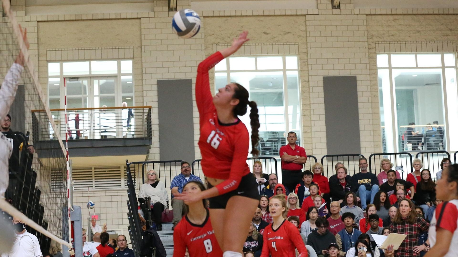 women's volleyball player wearing a red jersey jumping and swinging right arm at the ball
