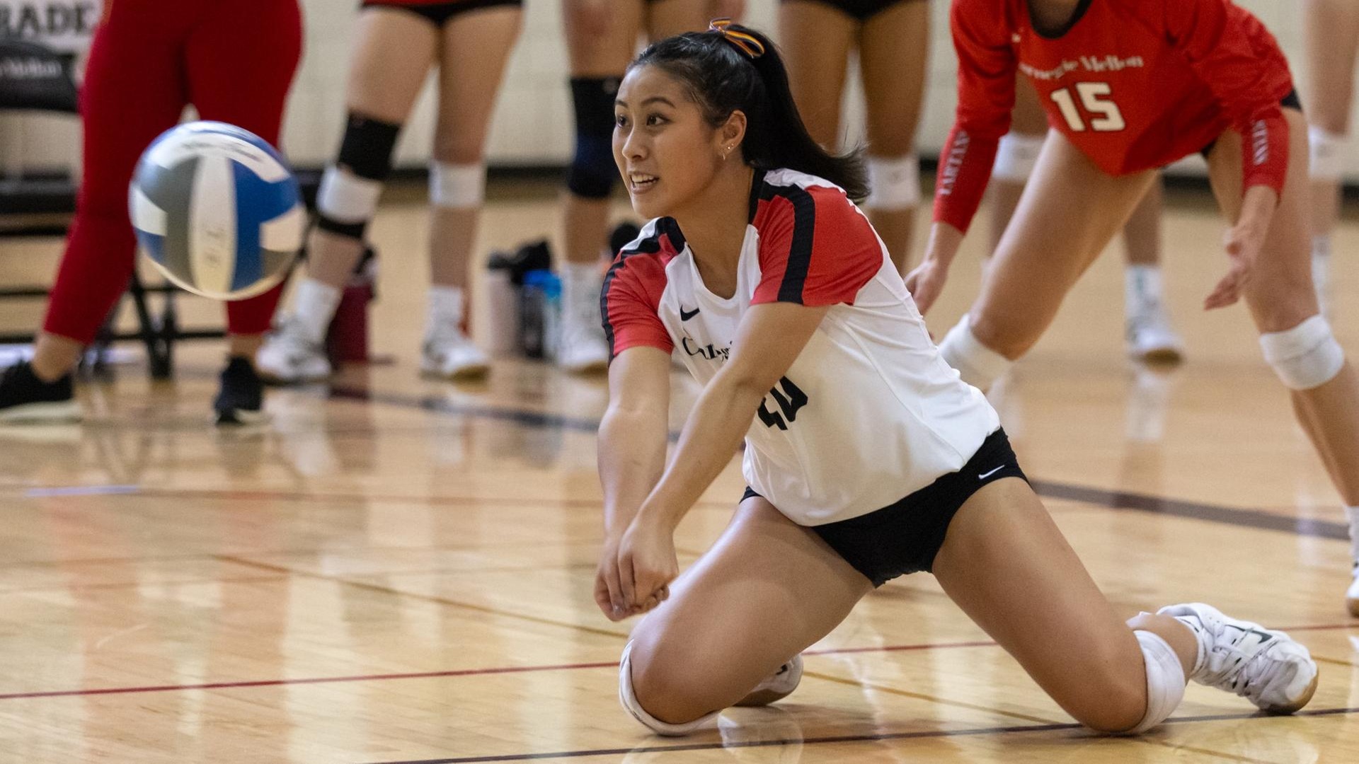 women's volleyball player wearing a white jersey kneels on ground to prepare to play a ball