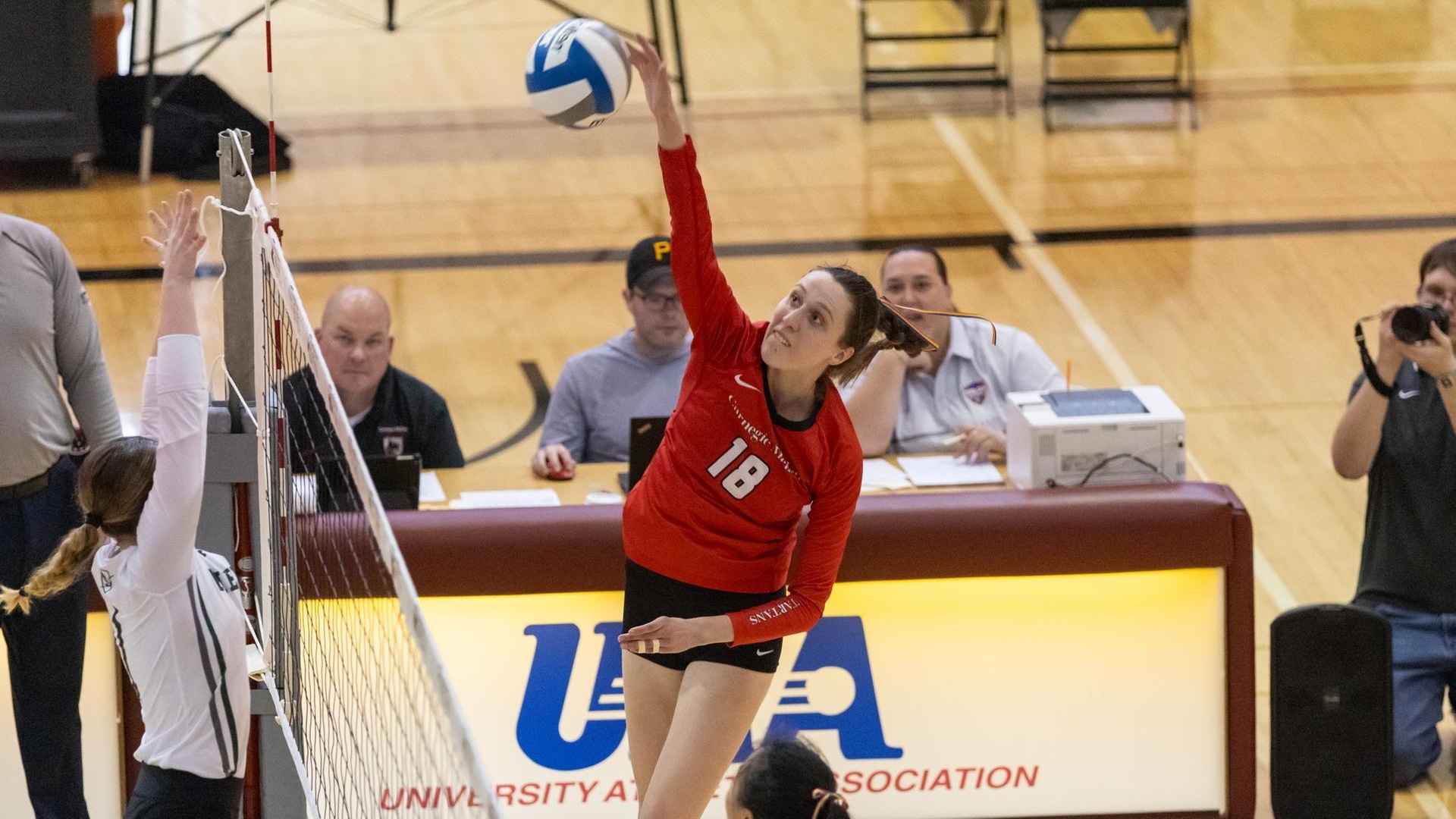 women's volleyball player wearing a red jersey makes contact with the ball with her right hand